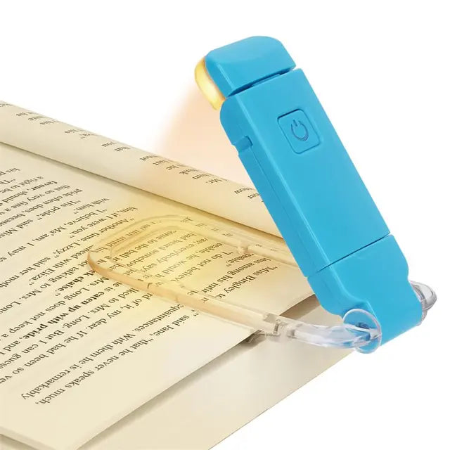 Blue clip-on LED book light attached to an open book, casting warm light onto the pages